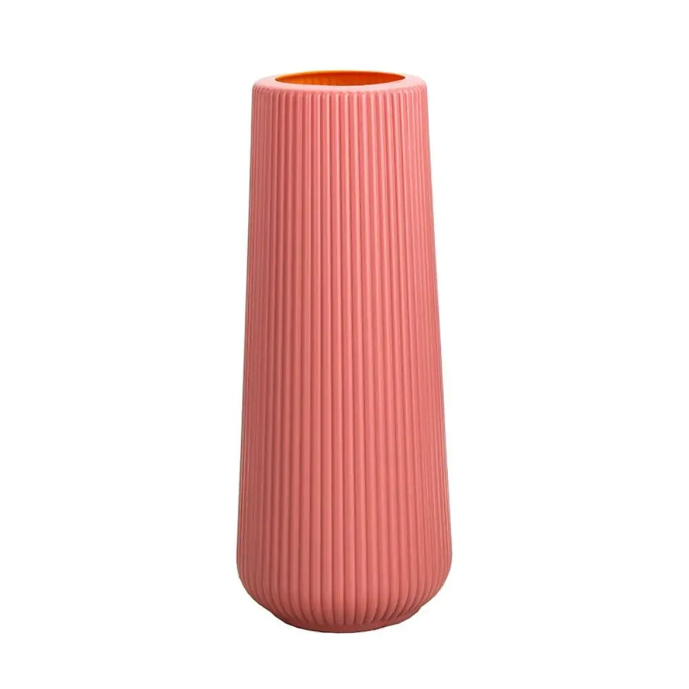 A tall, cylindrical plastic flower vase with vertical ribbed texture in a soft coral pink color.