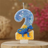 A birthday candle shaped like the number 2, decorated with blue glitter and a small dinosaur figure.