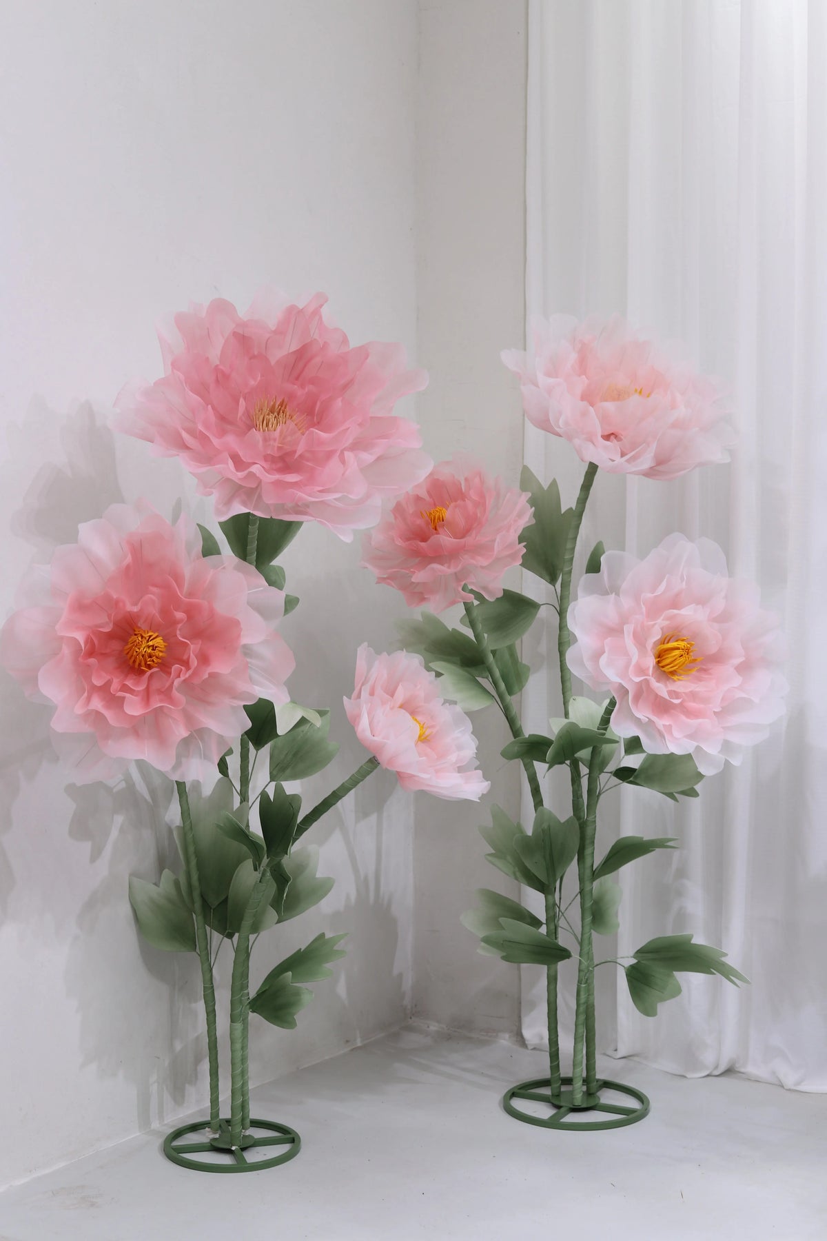 A large artificial silk pink poppy flower arrangement displayed on a green stand against a white background.