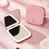 A pink portable folding LED makeup mirror with a black reflective surface is shown on a light pink background.