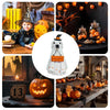 A white ghost figurine with a witch hat and a welcome sign displayed on a wooden surface surrounded by Halloween decor.