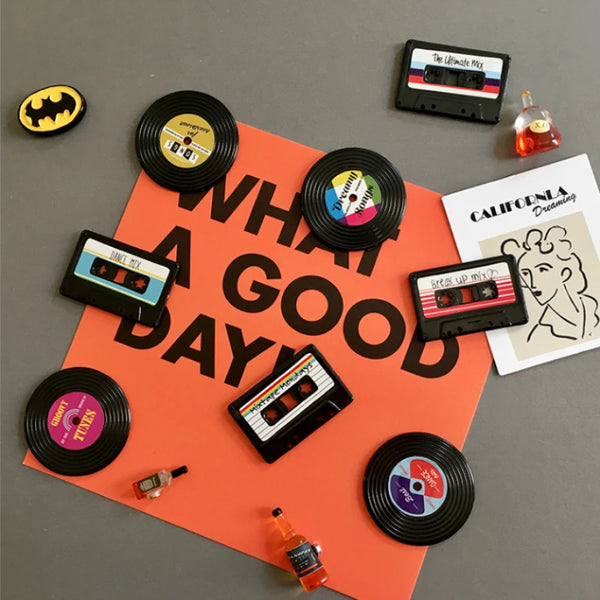 A set of four retro cassette tape fridge magnets in various colors and designs arranged on an orange background.