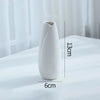 A white ceramic bud vase with an elongated, tapered shape is shown on a white surface.