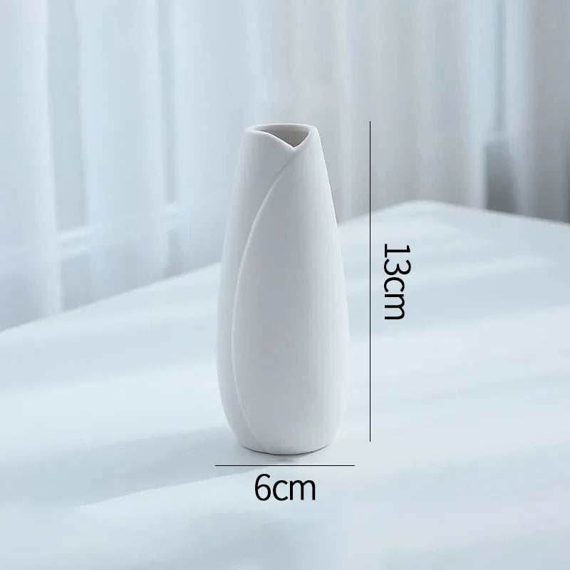 A white ceramic bud vase with an elongated, tapered shape is shown on a white surface.