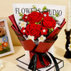 A bouquet of handcrafted red crochet roses with white accents displayed in a red ribbon and white wrapping.