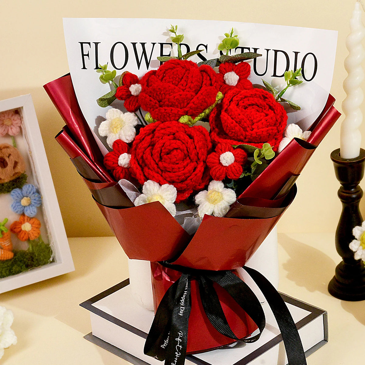 A bouquet of handcrafted red crochet roses with white accents displayed in a red ribbon and white box.