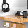 A black universal wall-mounted headphone holder and hanger displayed on a wooden desk surface.