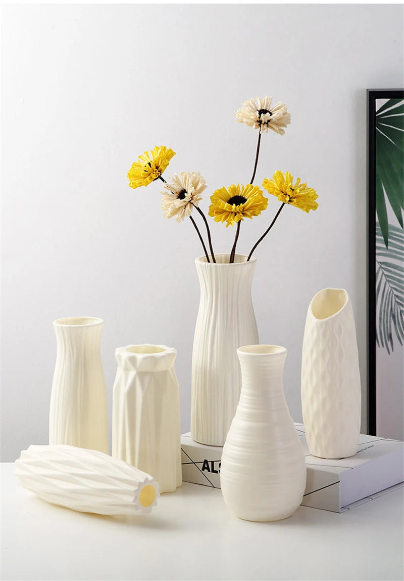 A white ceramic vase holds dried yellow and cream flowers against a light background.