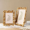 A golden 3D resin photo frame with a floral design is displayed on a wooden surface.