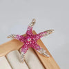 A vintage marine life brooch pin set featuring pink and silver glittery starfish shapes displayed on a light wooden surface.