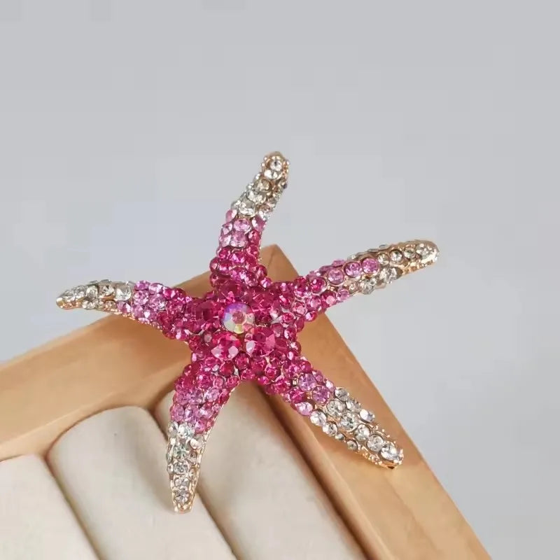 A vintage marine life brooch pin set featuring pink and silver glittery starfish shapes displayed on a light wooden surface.