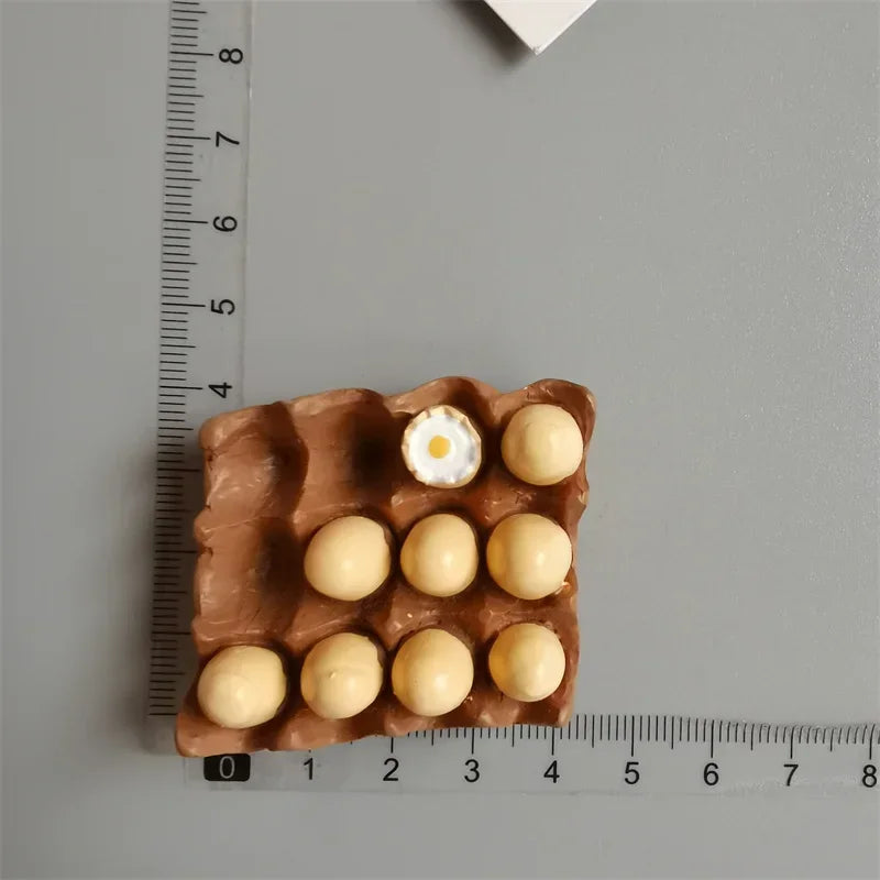 A set of playful food-shaped fridge magnets, including eggs and round yellow items, displayed next to a ruler.