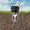 A black garden key hider tool with a pointed tip is shown inserted into dark soil.