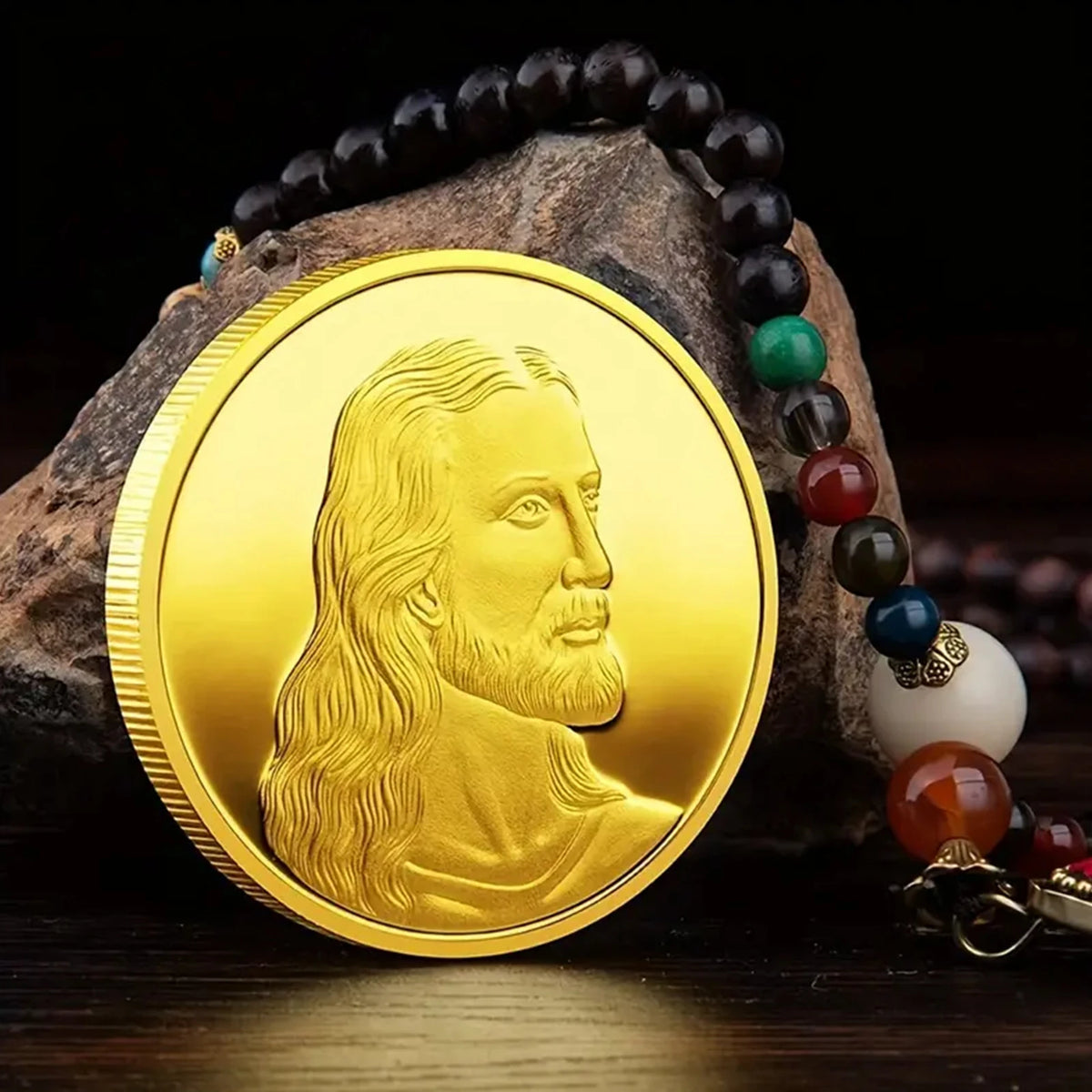 A gold commemorative metal coin featuring a profile of Jesus Christ, resting on a dark rock.