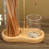 A wooden incense holder with a glass container filled with thin sticks and a separate glass cup for ash.