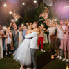 A couple is kissing under twinkling golden tinsel wedding wands with LED glow in a dark outdoor setting.