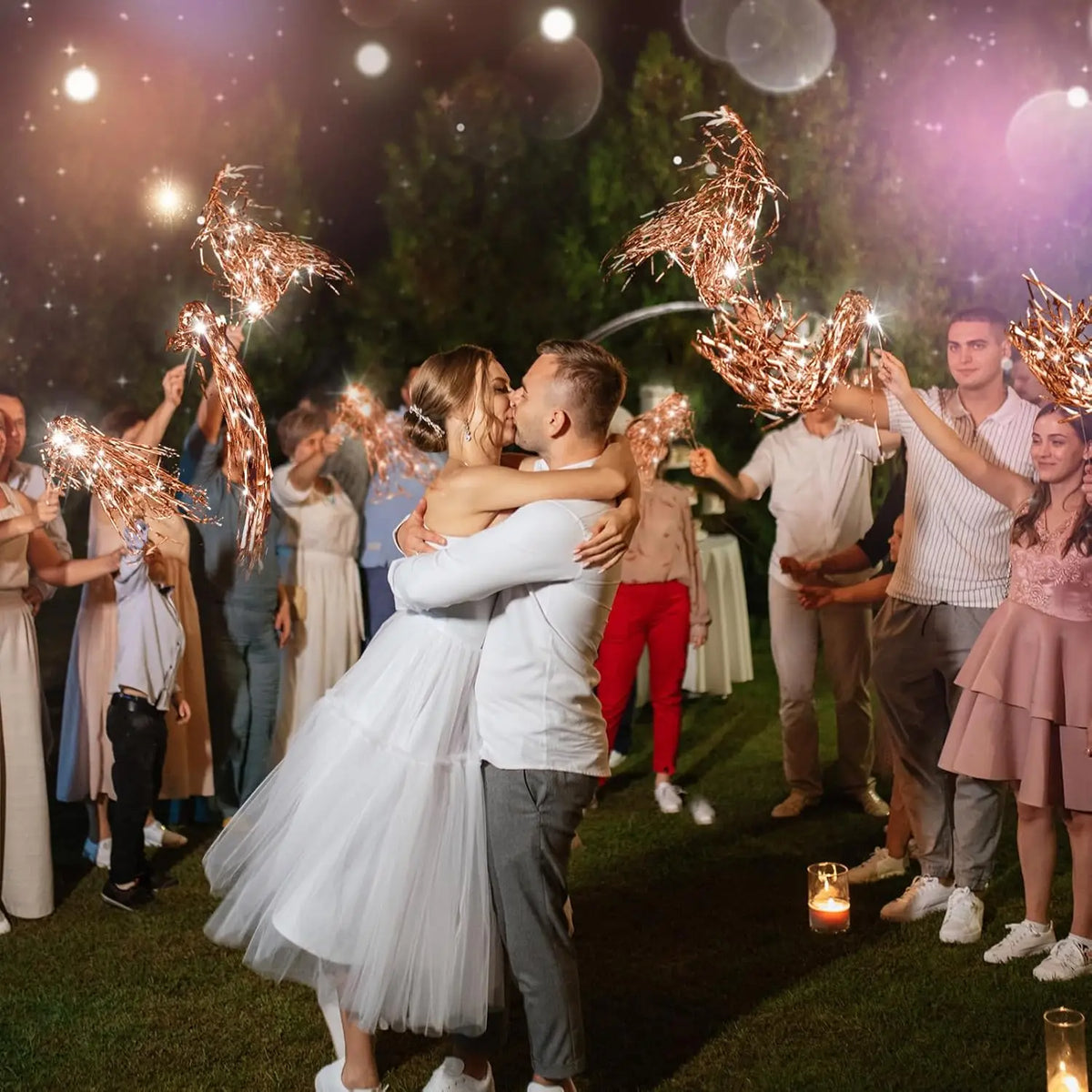 A couple is kissing under twinkling golden tinsel wedding wands with LED glow in a dark outdoor setting.