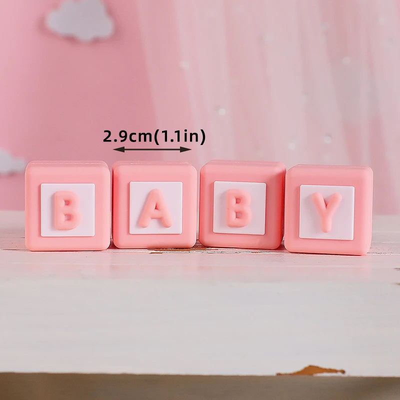 Four pink baby blocks with the letters B A B Y arranged in a row on a white surface.