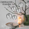 Silver disco balls are used for decoration, hanging from bare branches next to candles and a glass vase.
