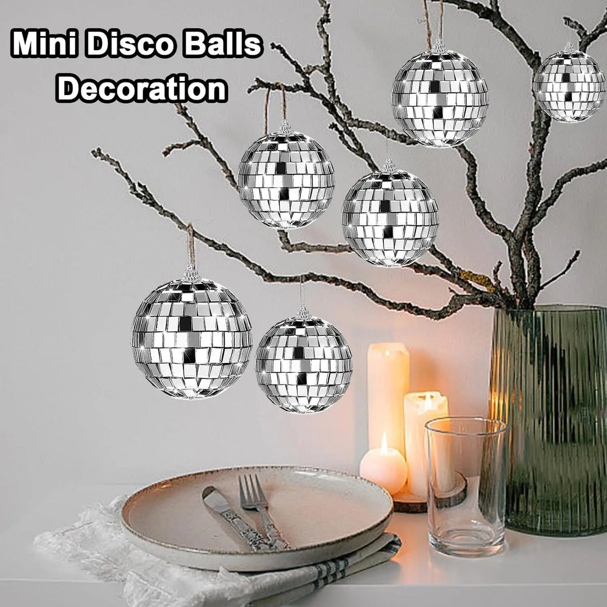Silver disco balls are used for decoration, hanging from bare branches next to candles and a glass vase.