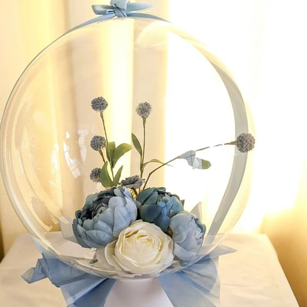 A clear spherical balloon filled with blue and white flowers tied with a light blue ribbon.