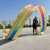 Un artista vestido de negro está dentro de un gran arco de utilería de danza de dragones hecho de tela de colores arcoíris.