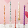 A collection of tall, decorative printed candles in peach, mint green, and lavender on a white surface.
