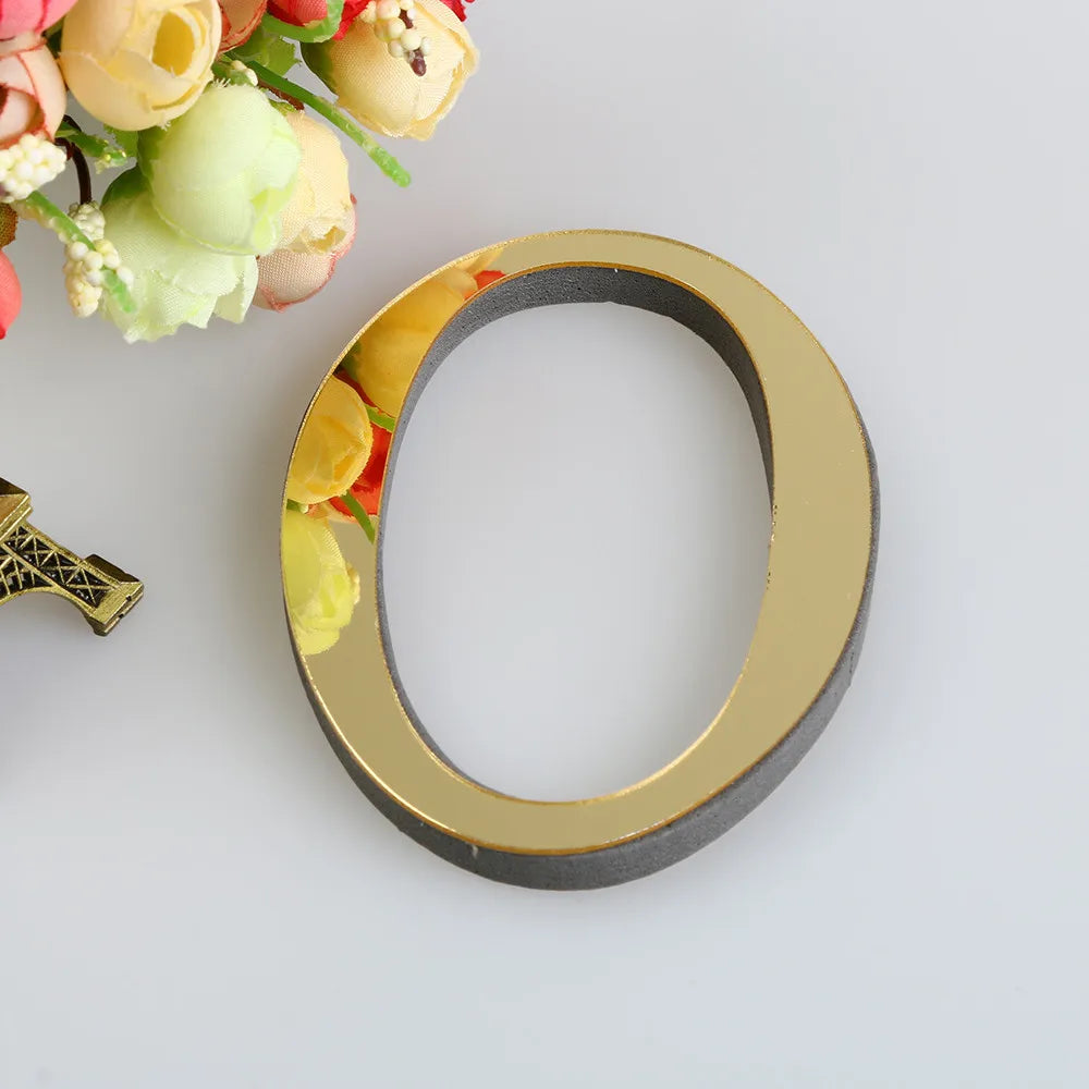 A circular gold letter mirror wall decal set with a dark gray rim and yellow floral accents.
