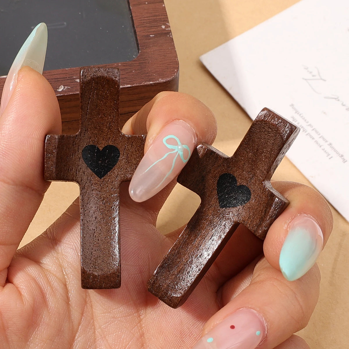 A hand holds a dark brown wooden pocket cross with a black heart carved into it.