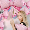 A woman is holding pink polka dot bow balloons for party decorations against a light background.