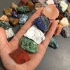 A hand holds a collection of assorted natural raw crystal stones and healing minerals on a dark surface.
