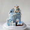 A light blue cake decorated with bear and car toppers, resting on a white cake stand.