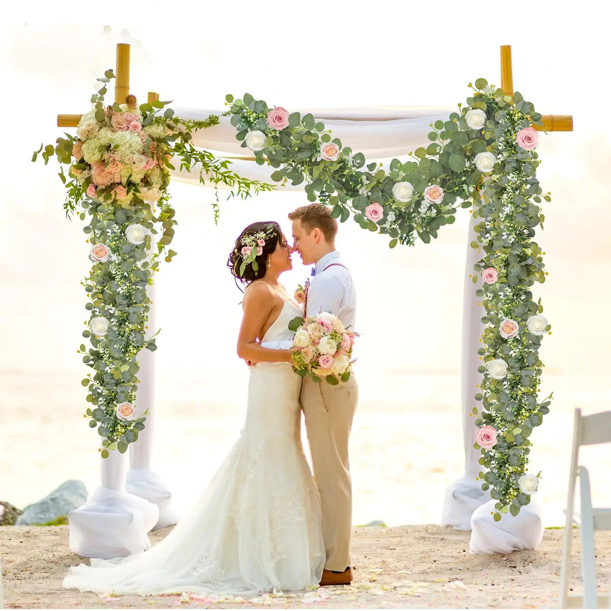 Un couple marié se tient sous une arche florale décorée de verdure et de roses pour une photo de mariage.