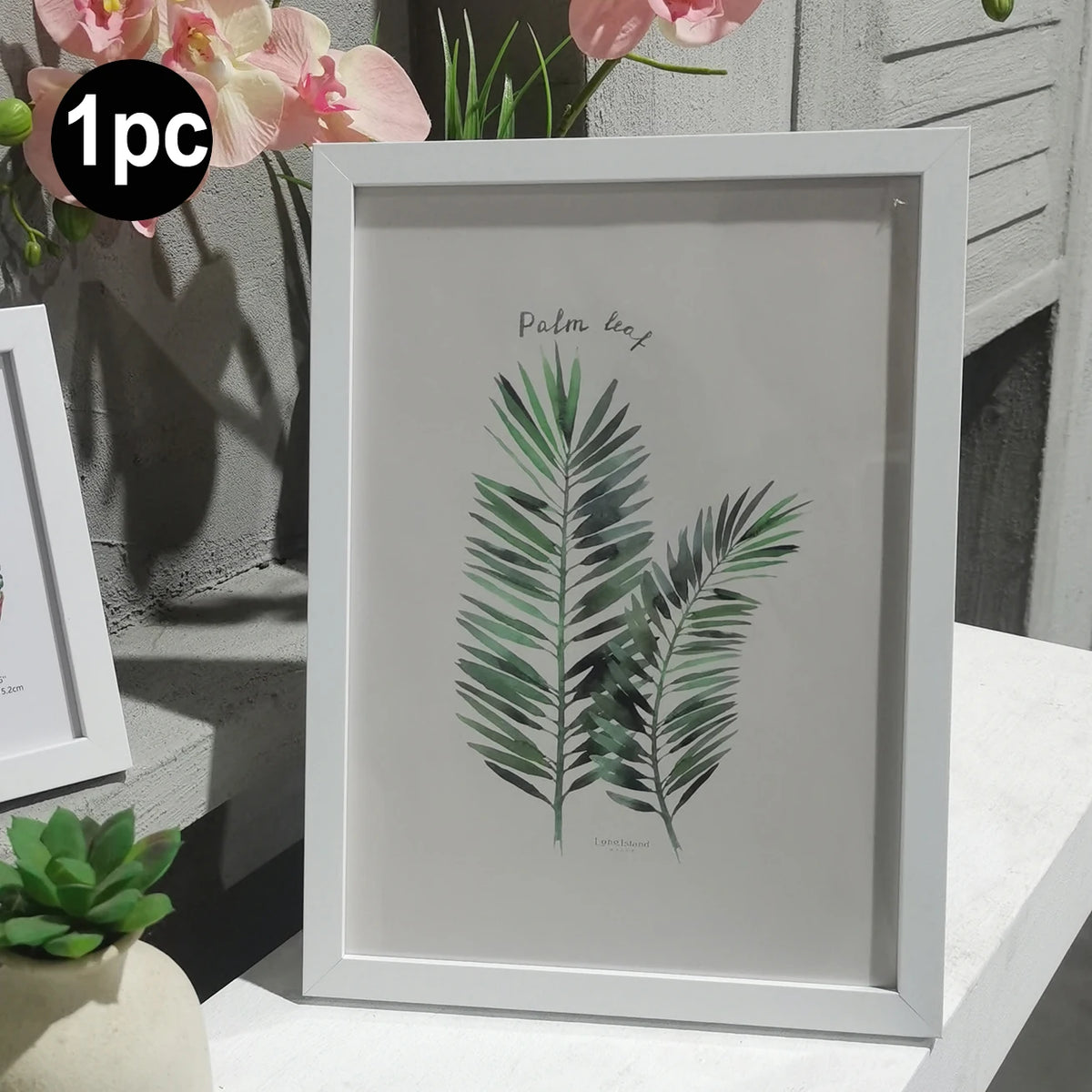 A framed botanical print featuring a green palm leaf on a white background.