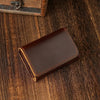 A dark brown leather card holder and cable organizer resting on a wooden surface.