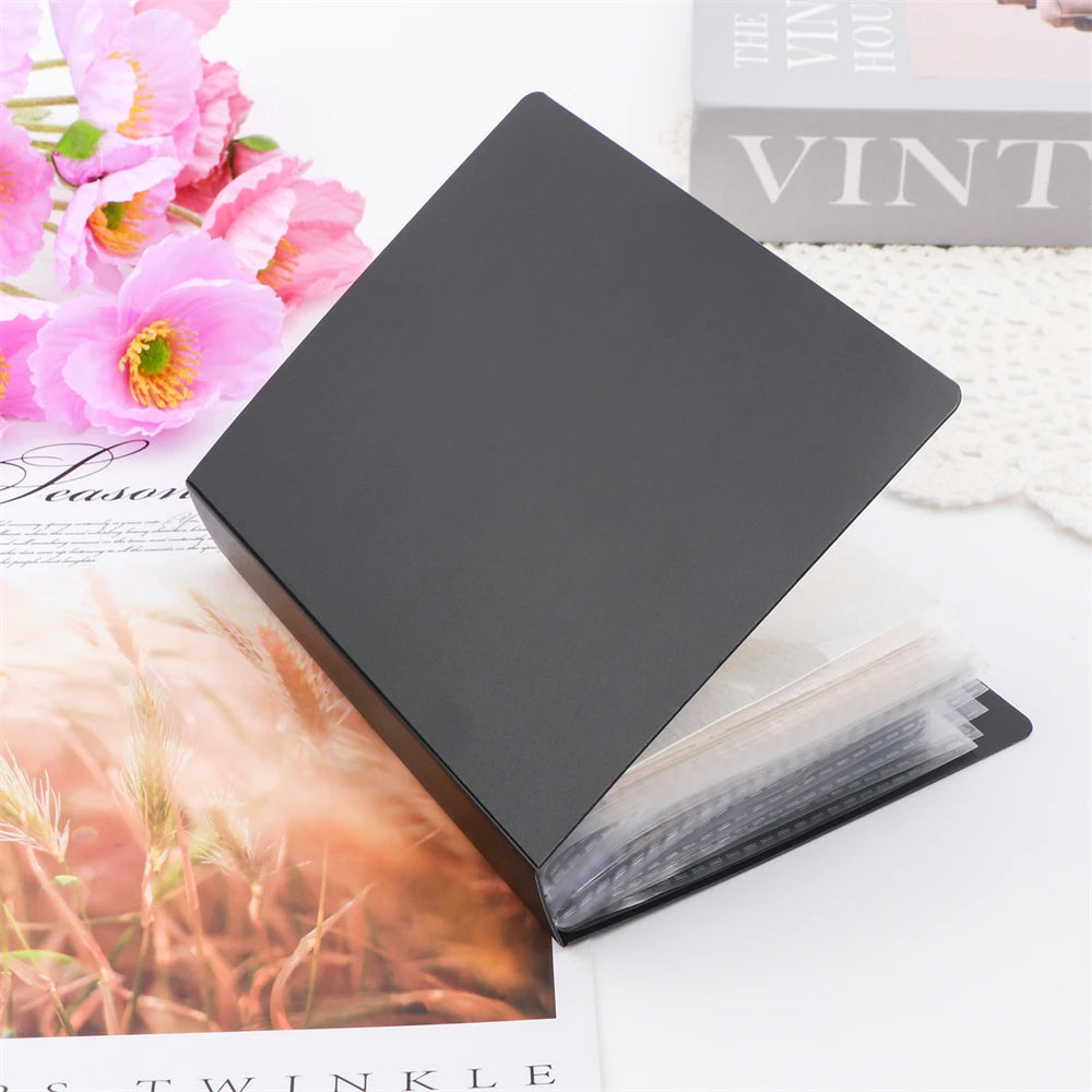 A black storage box with an open lid revealing clear pages for stickers, photos, and craft supplies.