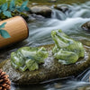 Une petite figurine de grenouille de jade verte translucide repose sur une roche moussue dans un ruisseau.