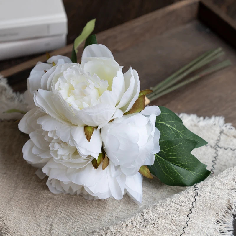 A bouquet of elegant white artificial silk peonies resting on a beige linen fabric.
