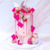 A pink cake decorated with pink and gold butterfly toppers and dripping icing on a white cake stand.