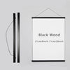 A vertical black magnetic wooden art frame with a white print, shown next to its hanging wire.