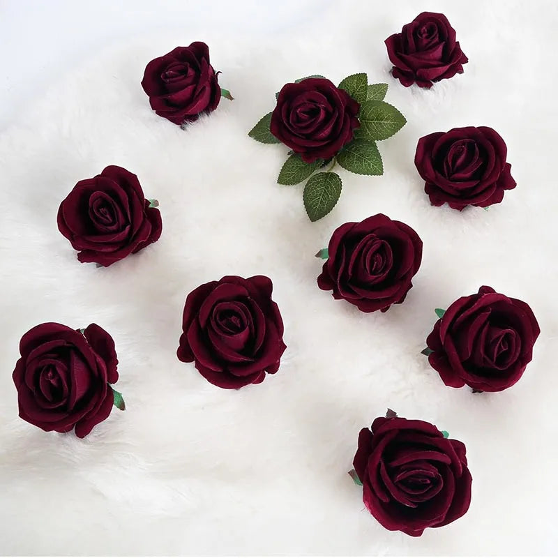 A collection of deep burgundy velvet artificial roses scattered on a white fluffy surface.