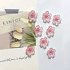 Pink and white decorative cherry blossom fridge magnets arranged on a light-colored card.