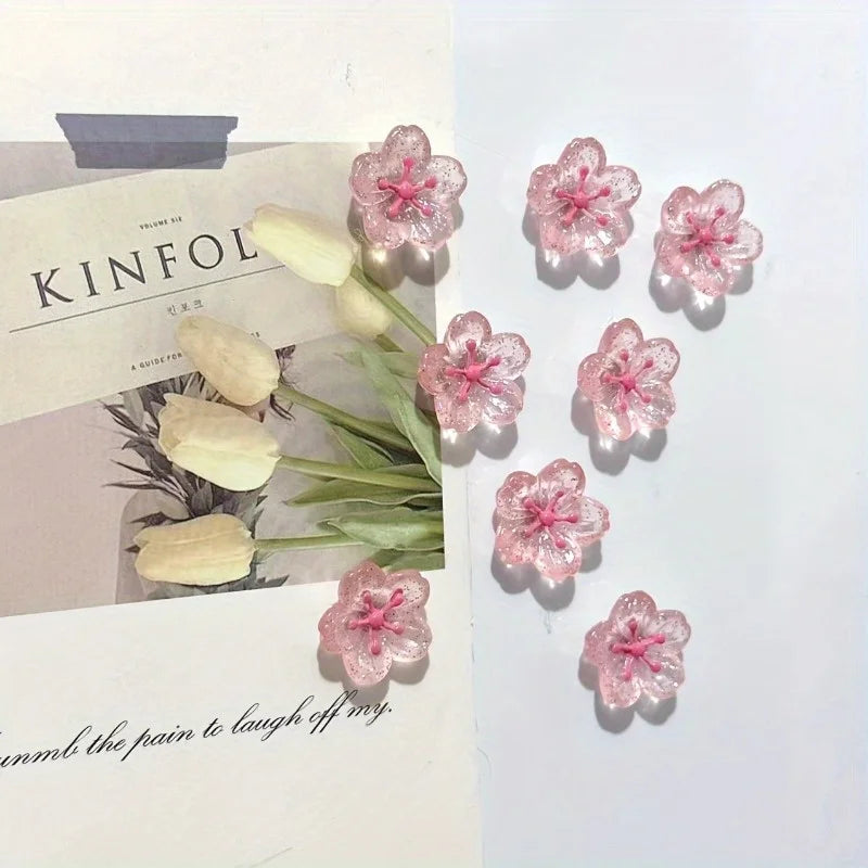 Pink and white decorative cherry blossom fridge magnets arranged on a light-colored card.