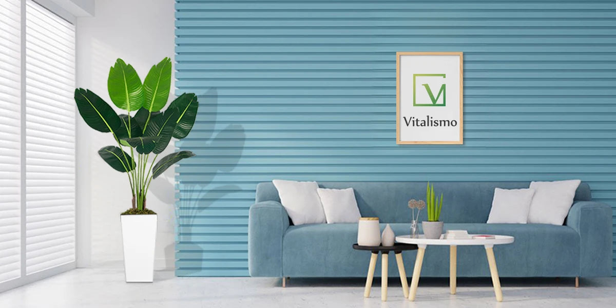 A green artificial Bird of Paradise plant in a white planter sits on a light blue sofa in a modern living room.