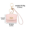 A light pink mini leather openable bag with a gold chain keychain and attached leather strap.