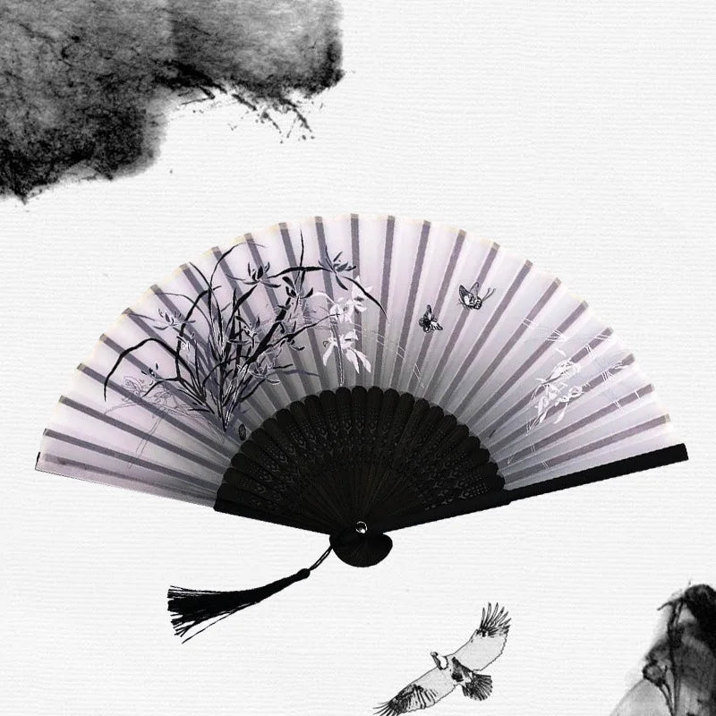 A black and white photograph of a vintage bamboo folding hand fan with delicate plant details and a small bird flying nearby.