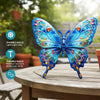 A vibrant blue metal butterfly wall art decoration with iridescent details displayed on a wooden table.