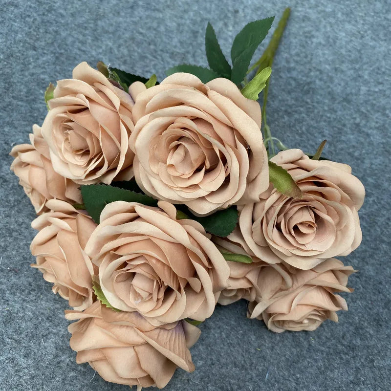 A bouquet of nine realistic silk roses in a soft peach or blush color with green leaves.