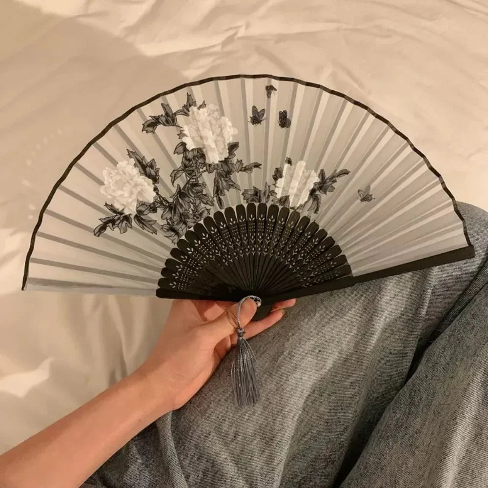A folding hand fan with a gray and black striped design and white floral print is held by a person.