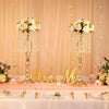 A set of gold crystal vases used as wedding centerpieces on a pink-draped table.